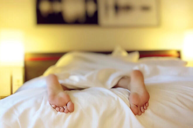 The bottom of a person's bare feet as they sleep in bed.