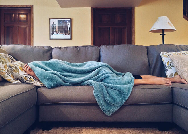 Person sleeping on couch with fuzzy blanket over their head.